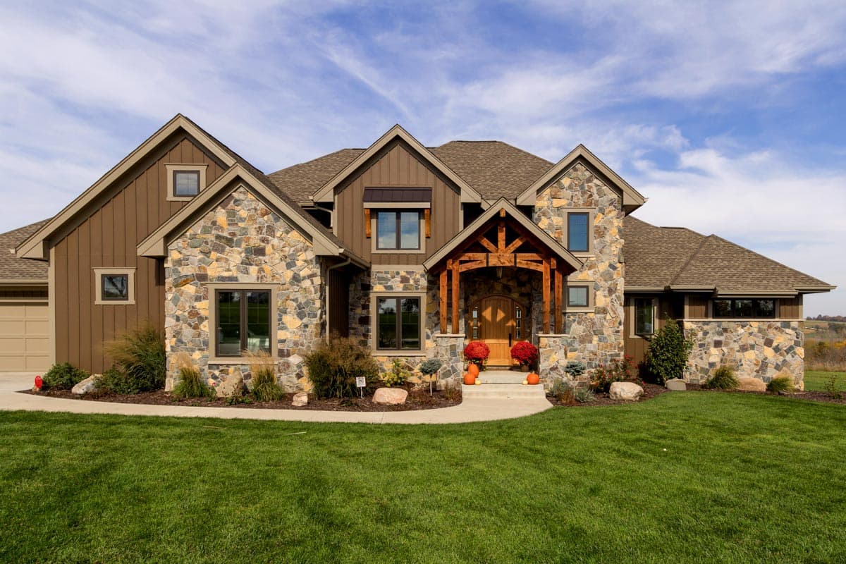 House plan exterior. Two-story home with stone and wood siding. Features include gabled roof, timber frame entry, and attached garage.