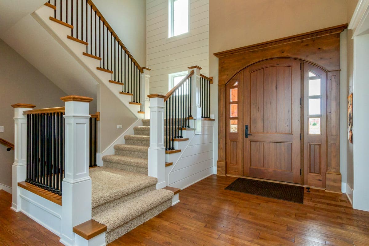Interior view of a foyer with a grand wooden double door, carpeted stairs with black spindles, and shiplap accent walls.