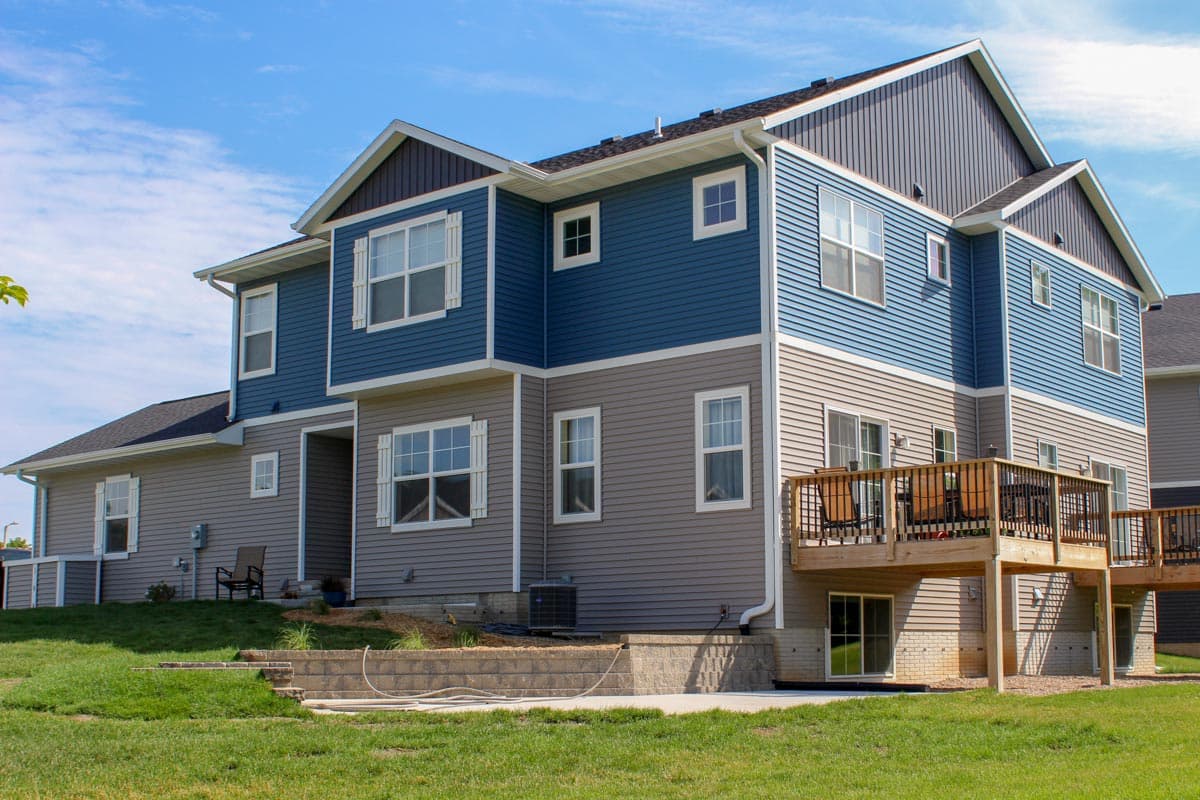 House plan exterior of a three-story home with blue and grey siding, multiple gables, a deck, and a grass yard.