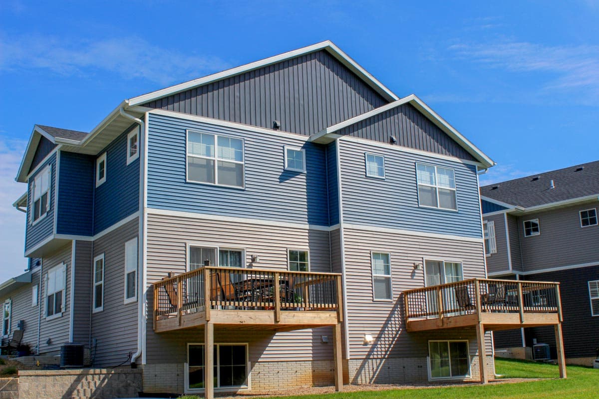 House plan exterior of a three-story building with blue and gray siding, multiple windows, and two decks.