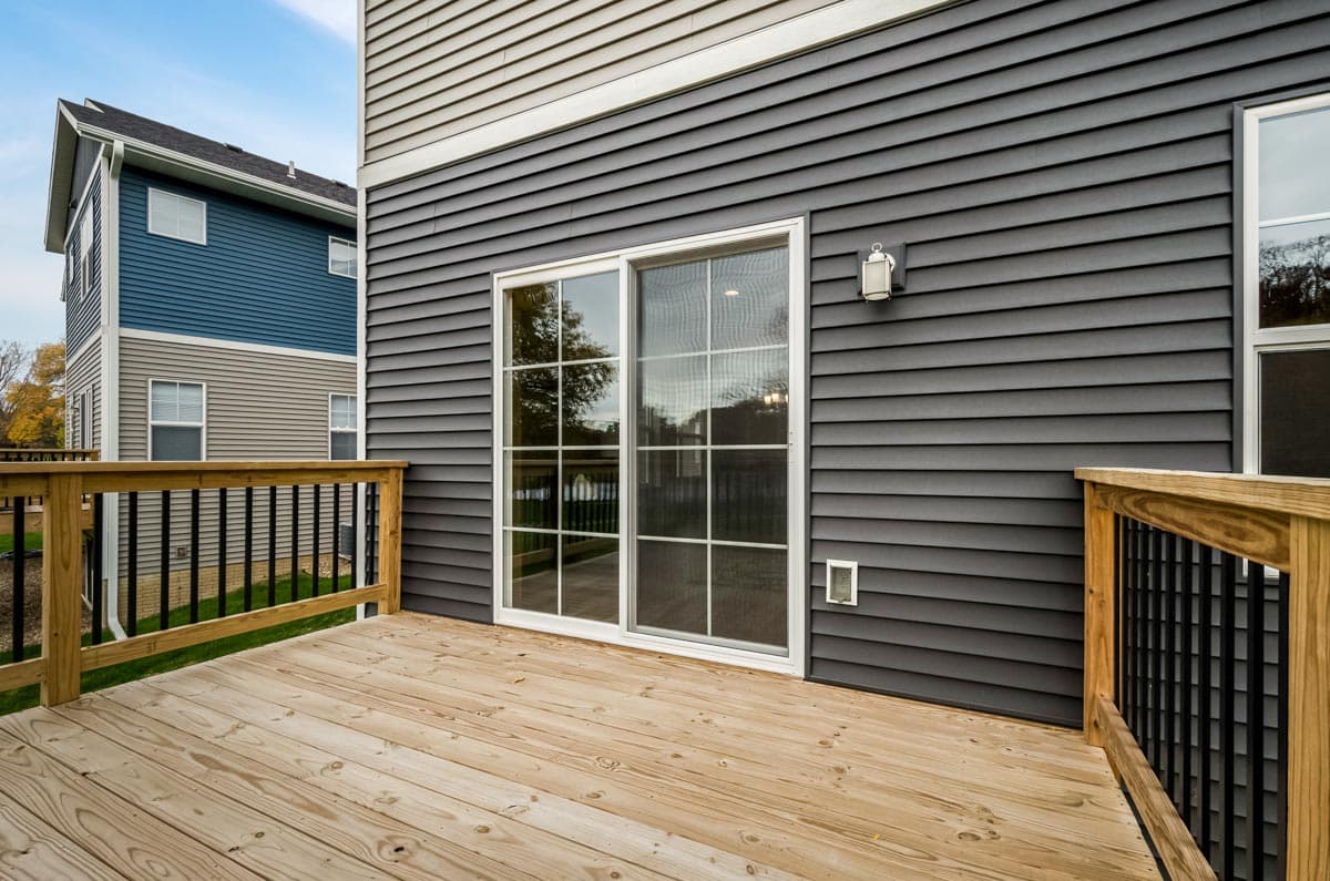 House plan exterior view of a multi-story building with gray siding, a wooden deck, and sliding glass doors.