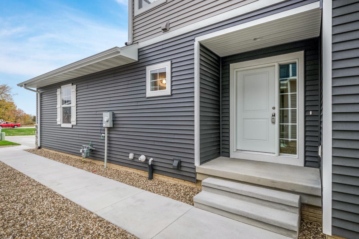 House plan exterior with gray horizontal siding, white-trimmed windows, and a covered entry with a white door.