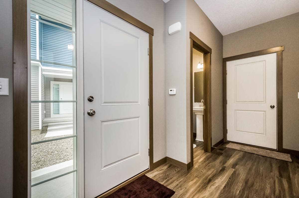 Interior view of house entrance, showing white panel door, glass sidelight, and doorway to powder room.