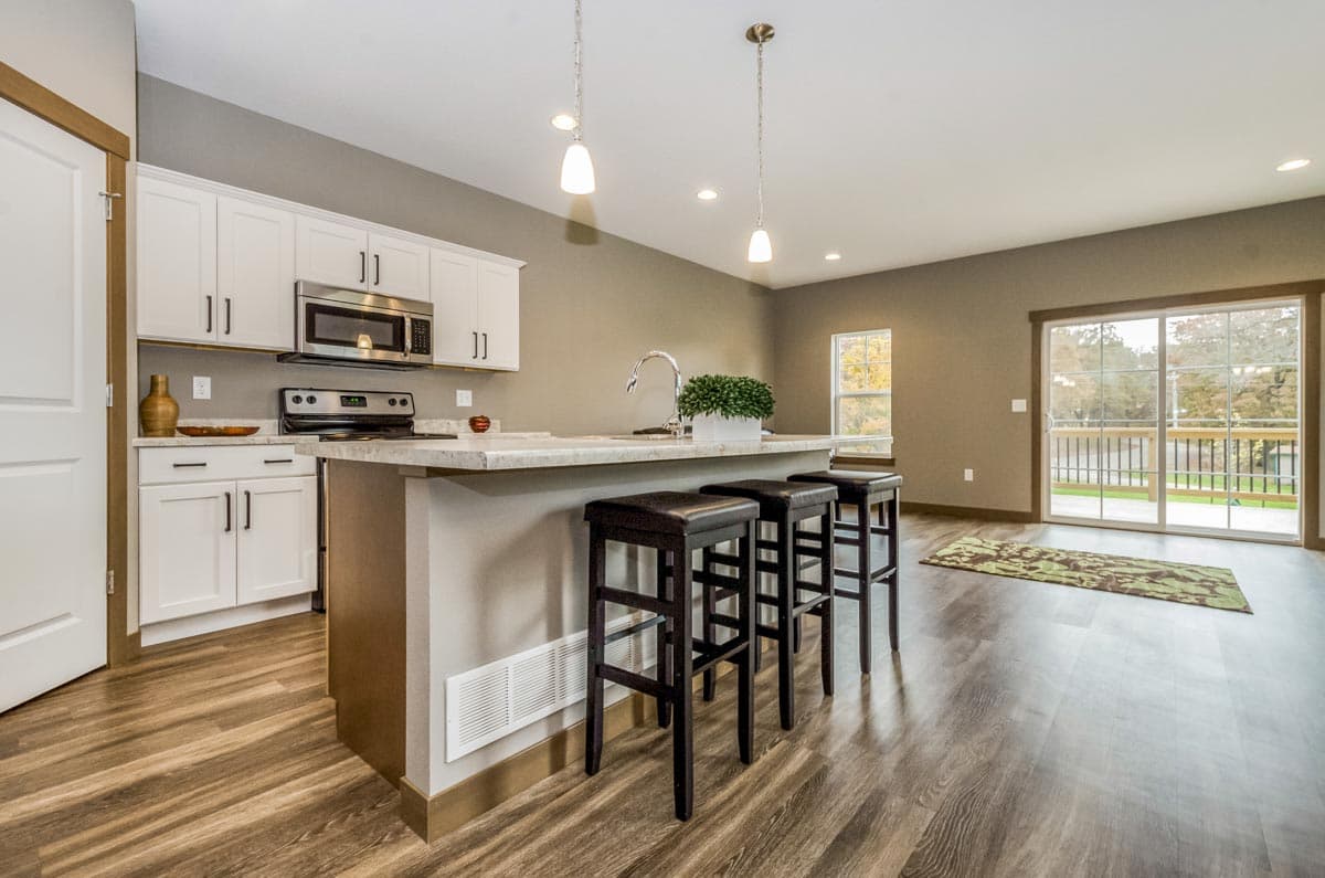 Kitchen with white cabinets, island seating for three, and a sliding glass door leading to a deck.