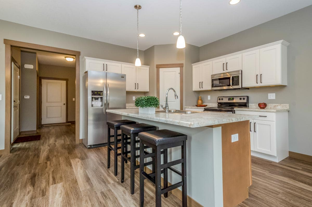 Kitchen with island, stainless steel appliances, white cabinetry, and pendant lighting. Adjacent hallway with doors visible.