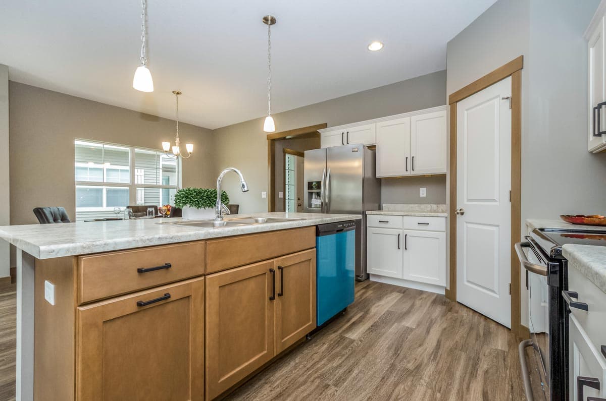 Kitchen interior with large island sink, stainless steel appliances, white cabinets, and wood-look flooring.