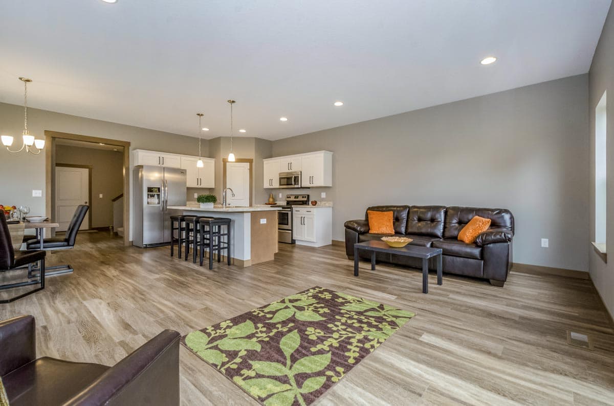Open concept living area with kitchen island, stainless steel appliances, dark leather sofa, and dining area.