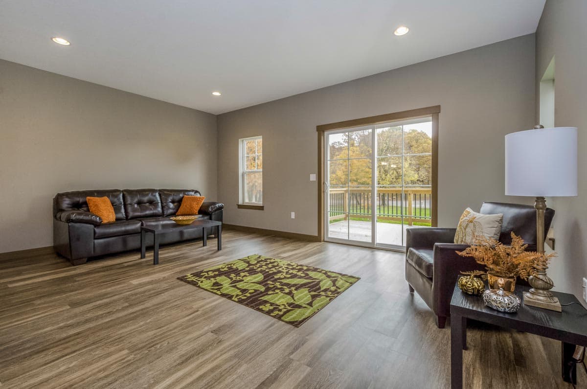 Living room with leather sofa, accent chair, sliding glass doors to deck, and wood-look flooring.