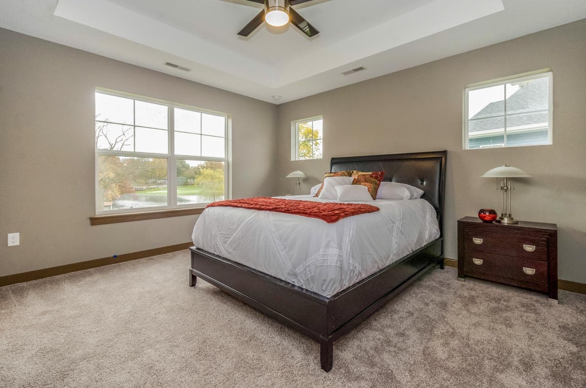 Primary bedroom with coffered ceiling, large windows overlooking water, and bed with headboard.