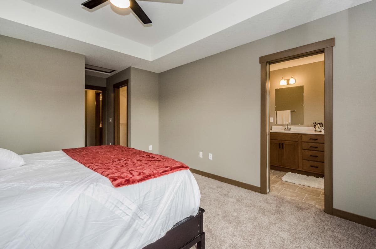 Bedroom interior with tray ceiling, ceiling fan, and doorway to bathroom featuring vanity and mirror.