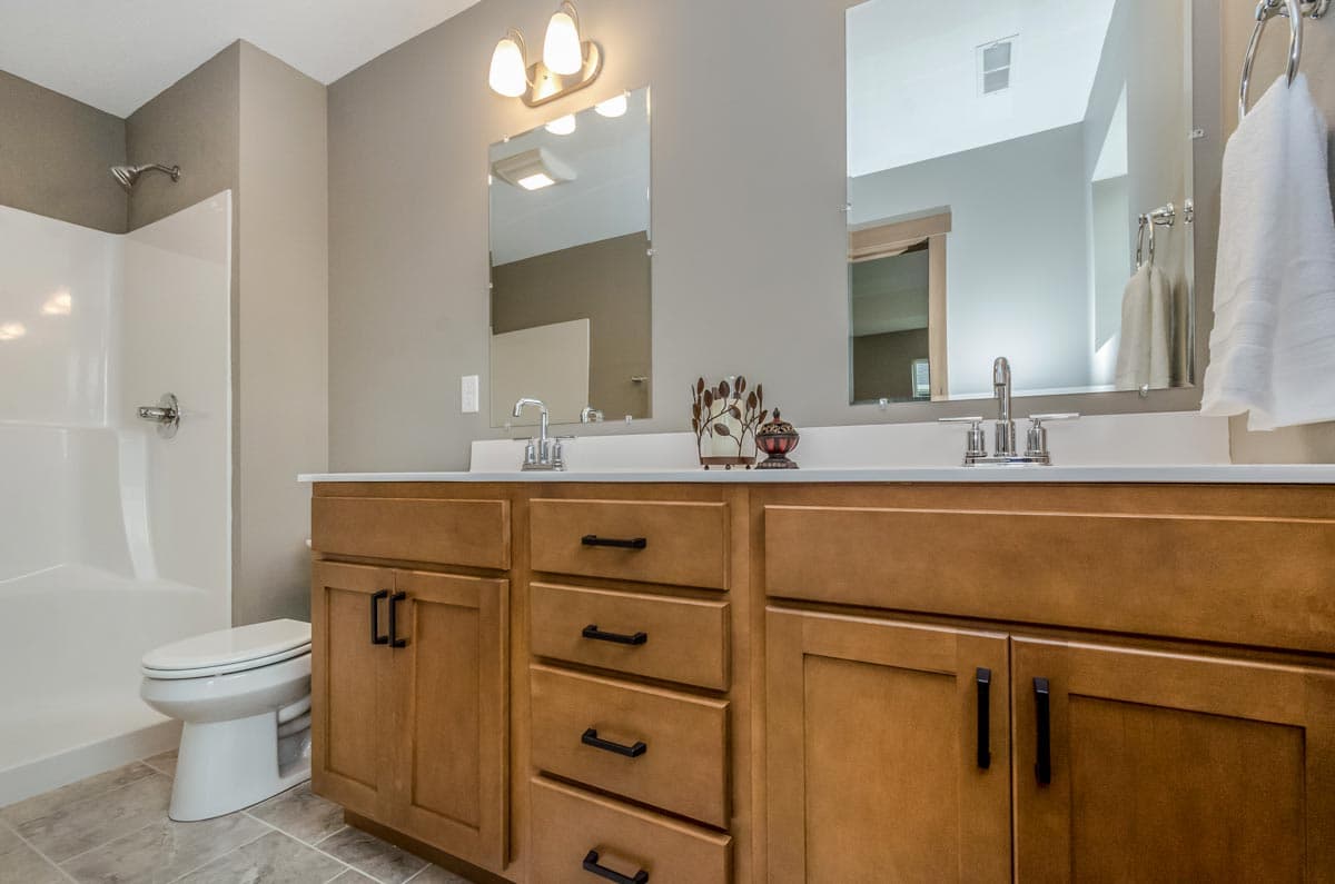 Bathroom with double vanity, natural wood cabinets, walk-in shower, and toilet.