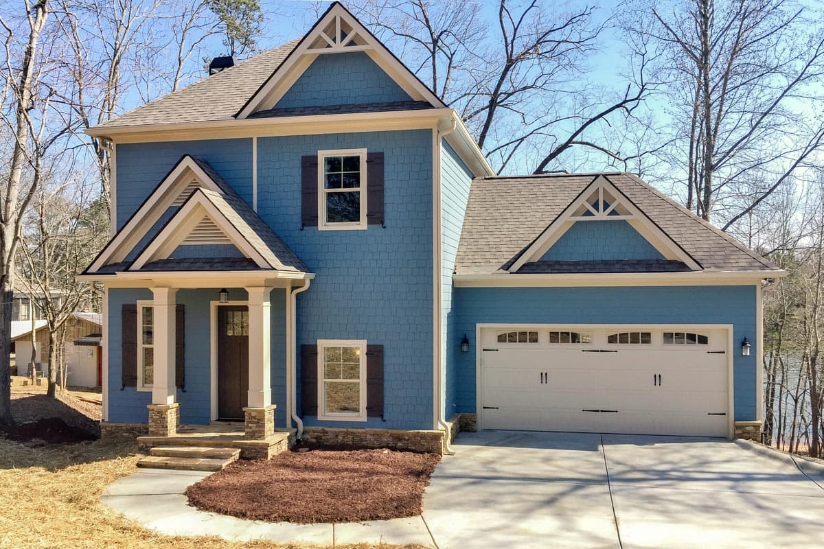 House plan exterior. Two-story Craftsman home with gabled roof, front porch, and garage. Features wood-shuttered windows and decorative trim details.