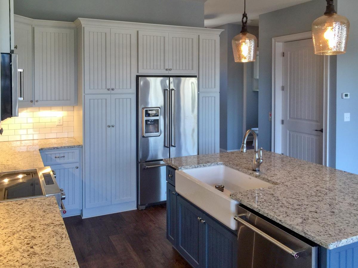 Kitchen with inset beadboard cabinets, stainless steel refrigerator, granite countertops, and an island with farmhouse sink.