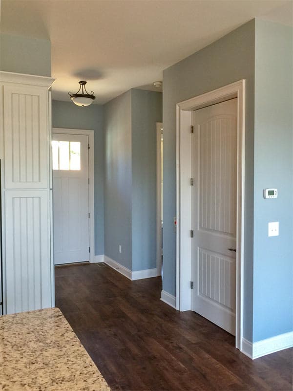 Interior hallway with paneled doors, beadboard cabinets, dark wood floors, and a decorative ceiling light fixture.