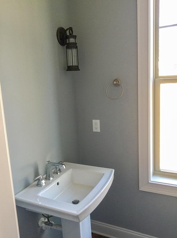 Pedestal sink with chrome faucet, wall-mounted lantern light, and towel ring in a gray-walled room with a window.
