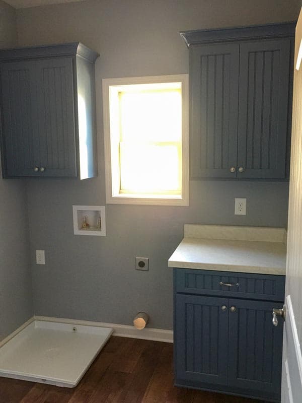 Laundry room with blue shaker cabinets, utility sink, window, and connections for washer and dryer.