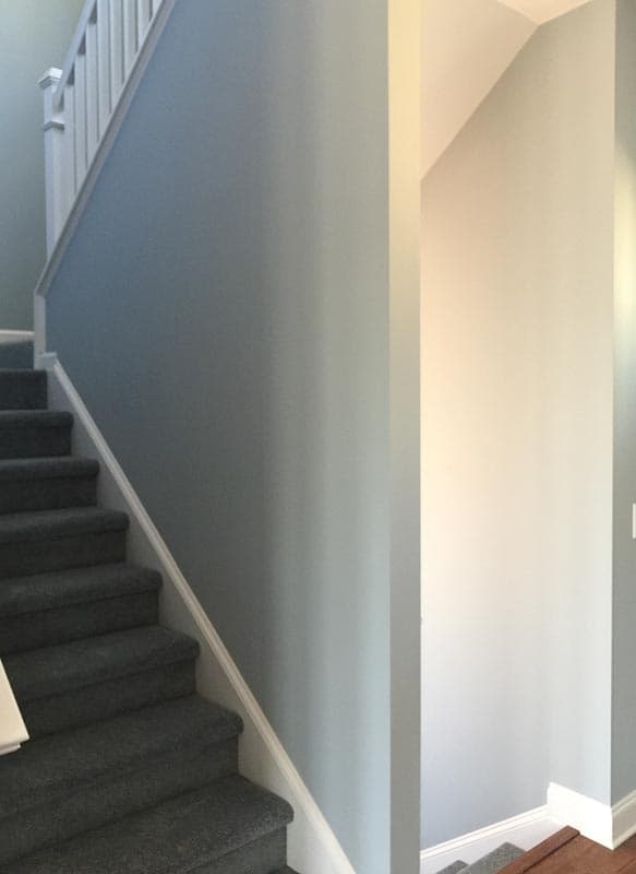 Interior view of a staircase with gray carpeted steps and white balusters. Light blue walls.