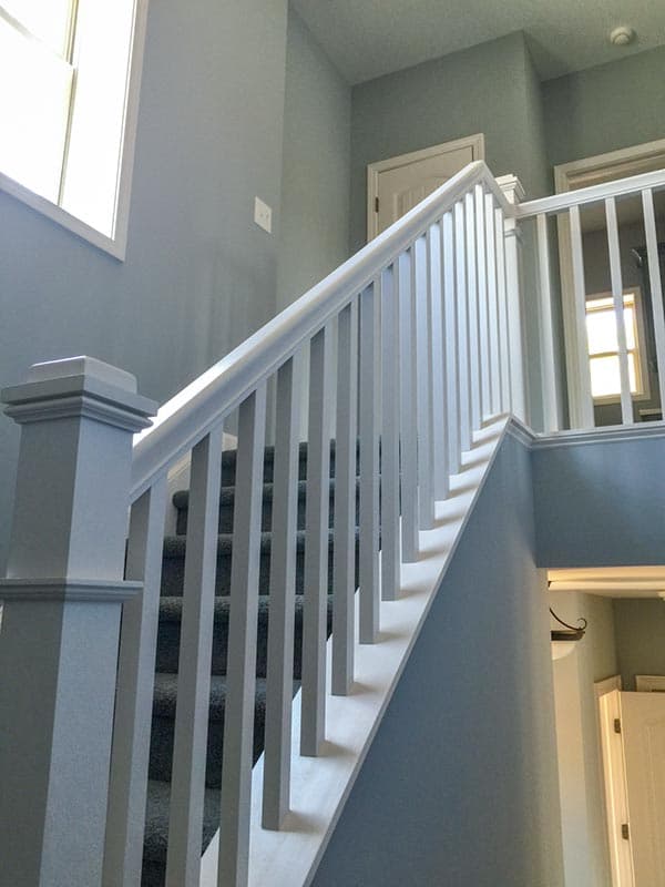 Interior view of a carpeted staircase with white balusters and handrail, leading to upper level with doors and window.
