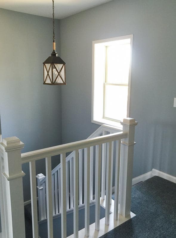 Interior view of a staircase with white railings, a hanging lantern, and a window.