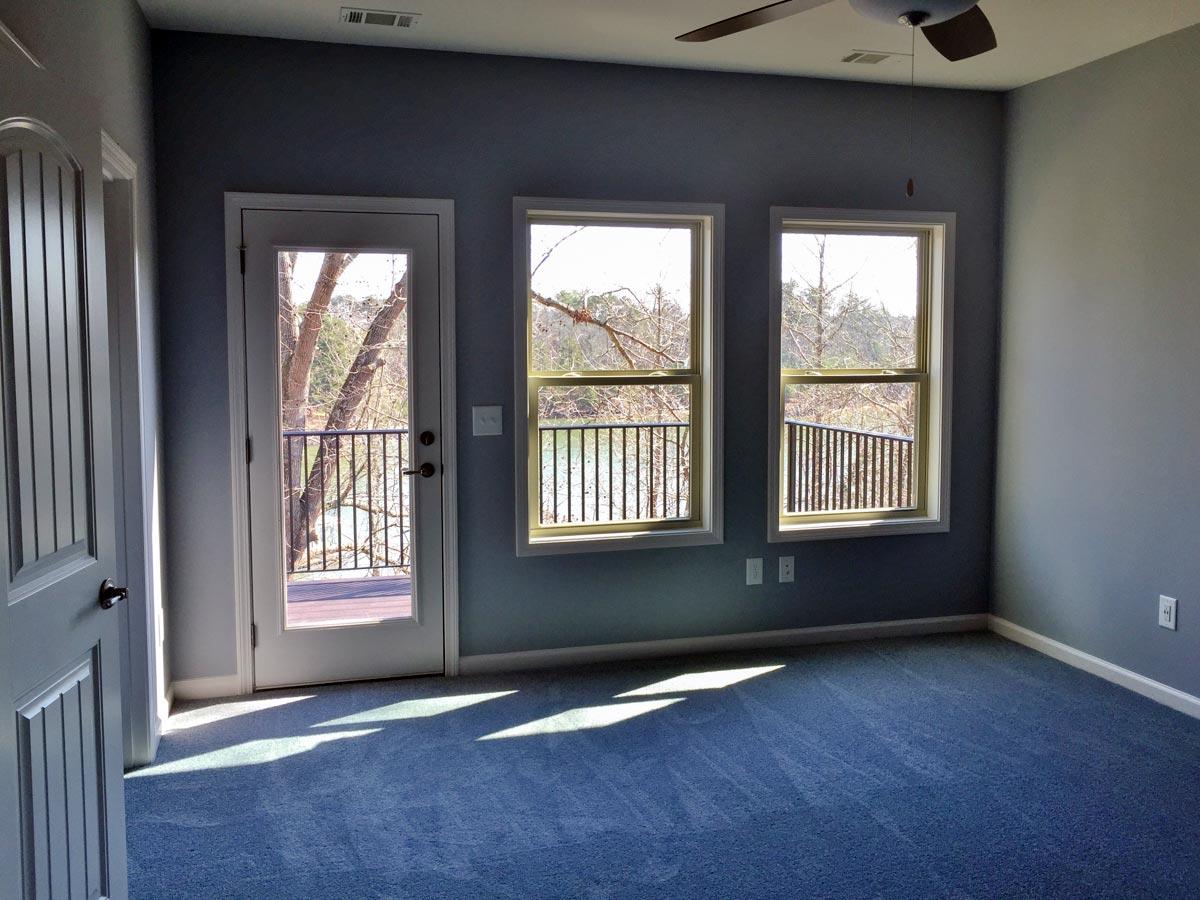 Interior view of a room with a door to a balcony, three windows, and a ceiling fan.