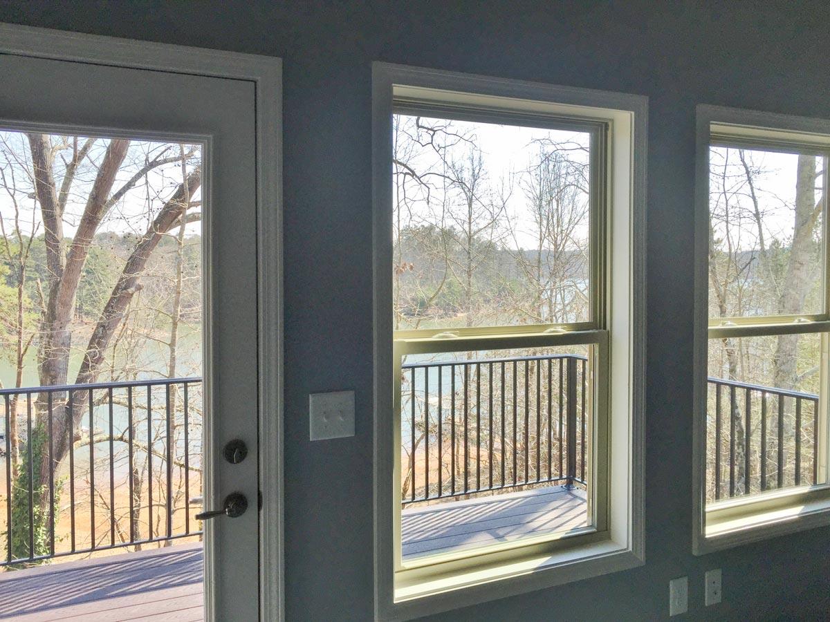 Interior view of a room with a door and windows opening to a deck and water view. Black metal railings visible.