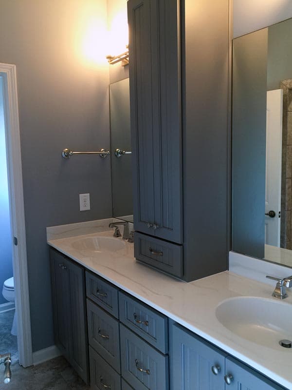 Bathroom vanity with dual sinks, white quartz countertop, gray shaker-style cabinets, and a tall linen cabinet.