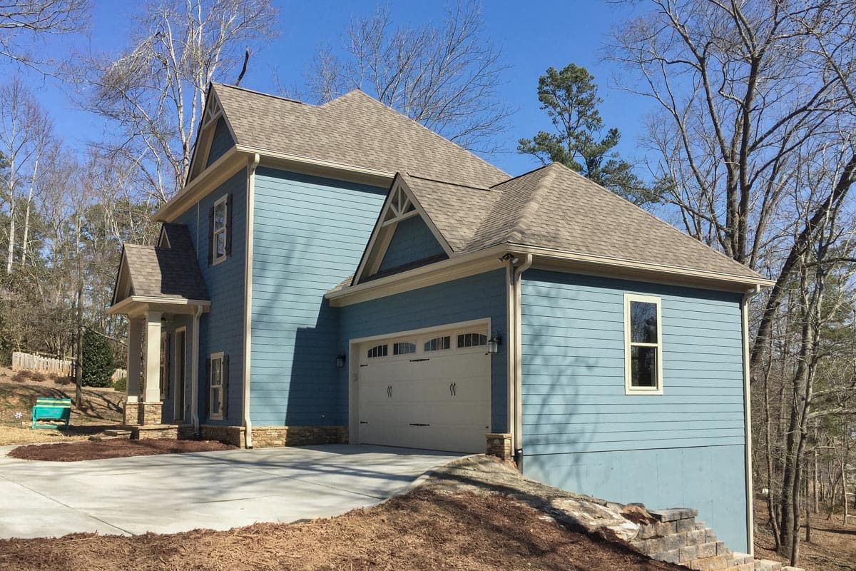 House plan exterior: Two-story blue home with gable roof, stone accents, front-facing garage, and covered front porch.
