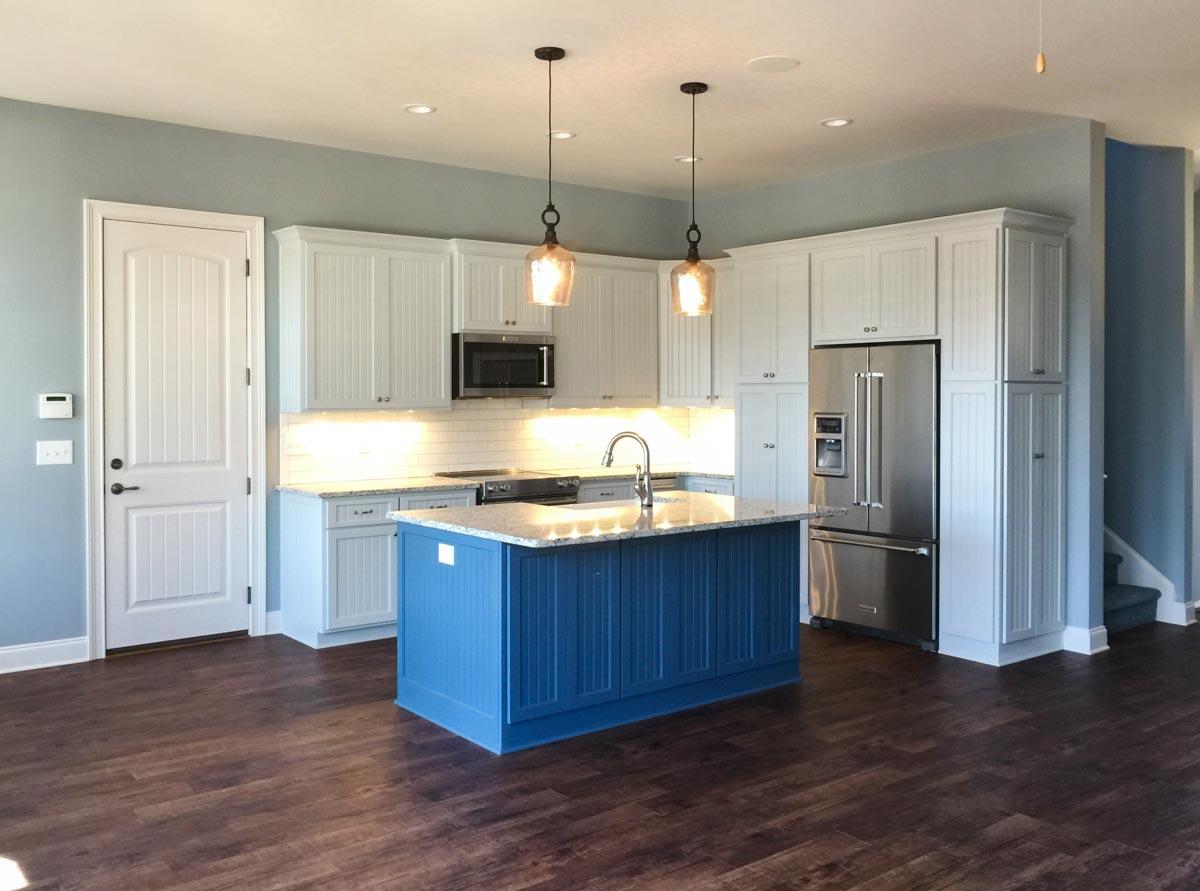 Kitchen with white beadboard cabinets, a blue island with granite countertop, stainless steel appliances, and dark wood flooring.