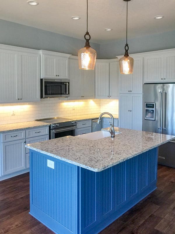 Kitchen with white beadboard cabinets, granite countertops, stainless steel appliances, and a blue island with a sink.