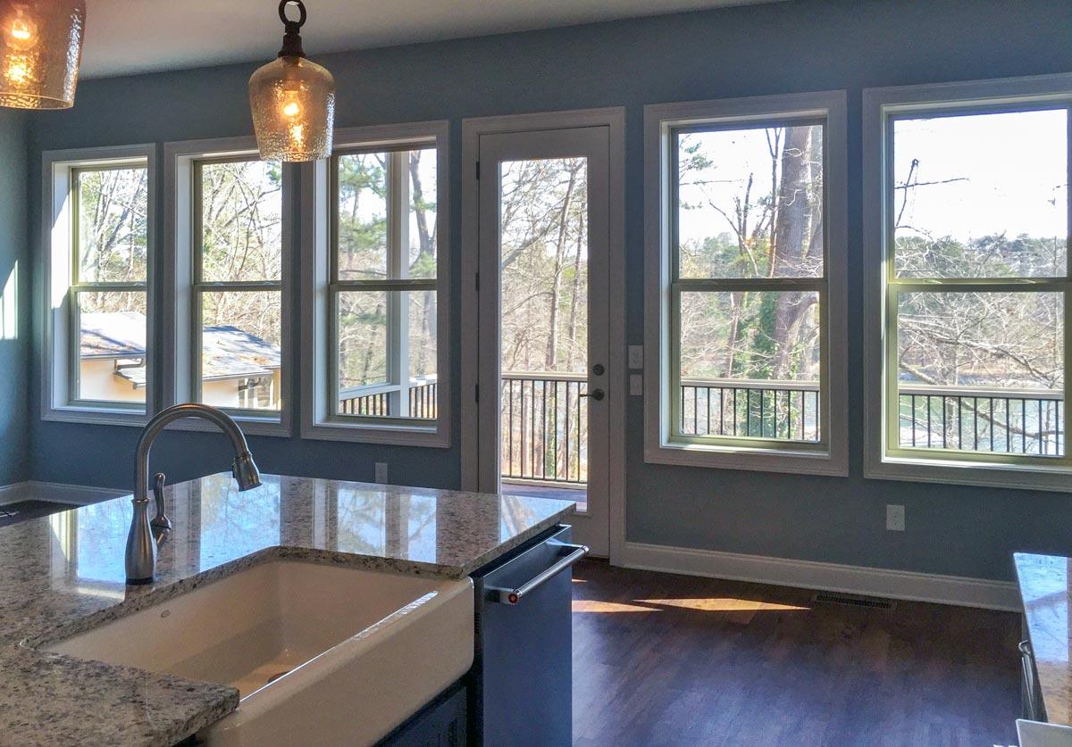 Kitchen with sink island, large windows, and a door leading to an outdoor deck with a railing.