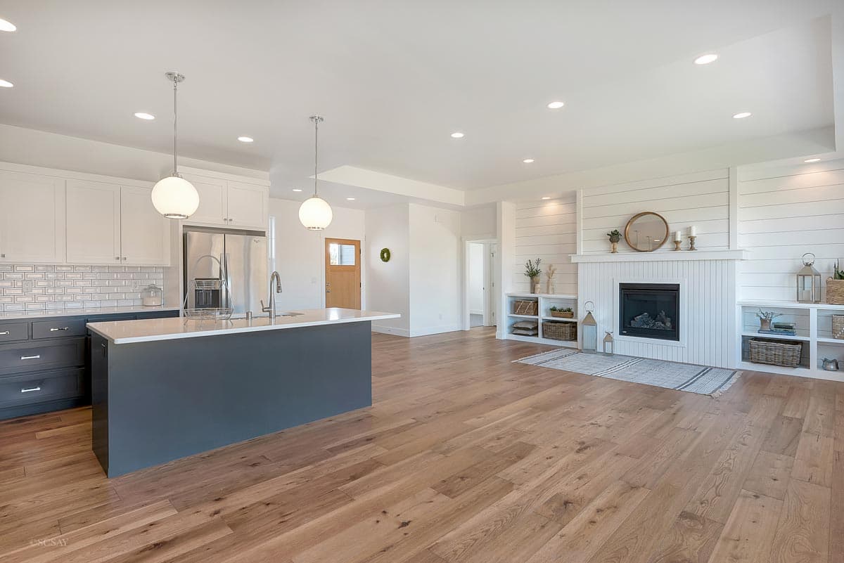 Open-concept living space with a kitchen island, shaker cabinets, and a shiplap fireplace with built-in shelving.