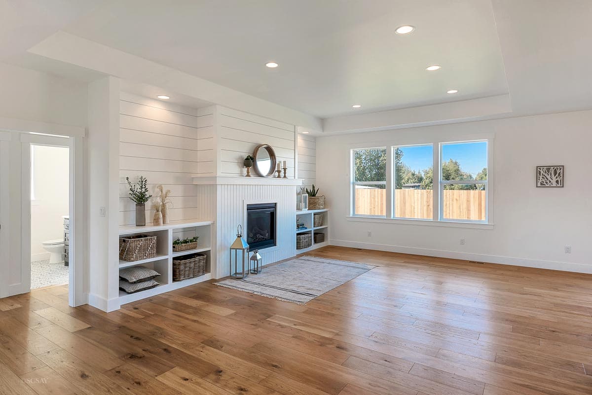 Interior view of a living room with shiplap fireplace, built-in shelving, and three large windows.
