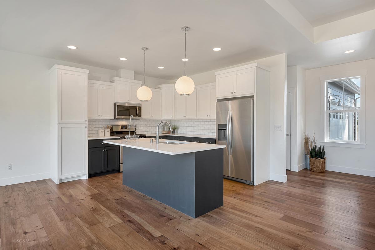 Open concept kitchen with white cabinets, dark lower cabinets, subway tile backsplash, island with sink, and stainless steel appliances.