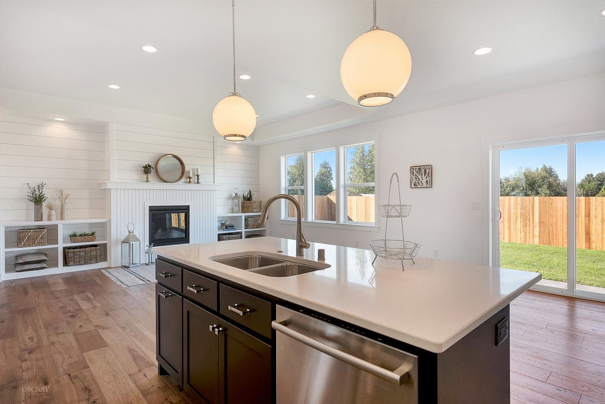 Kitchen with island, stainless steel dishwasher, fireplace, built-in shelving, and large windows.