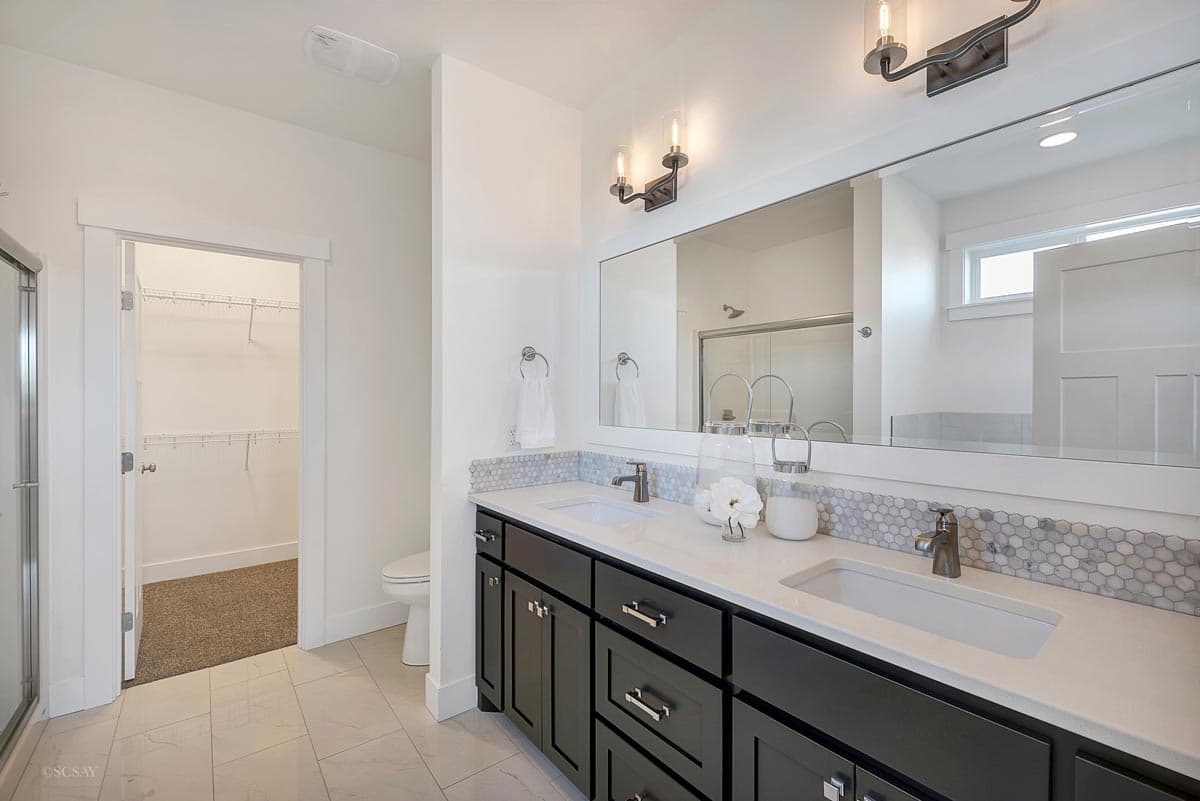 Bathroom with double vanity, walk-in closet, and tiled flooring. Vanity features dark cabinets and white countertops.