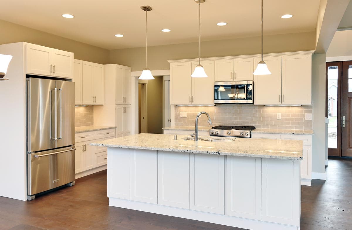 Contemporary kitchen with white shaker cabinets, a large granite island with sink, stainless steel appliances, and subway tile backsplash.