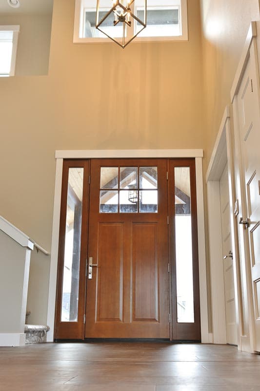 Modern wood front door with glass sidelights and transom window above in a two-story entryway.