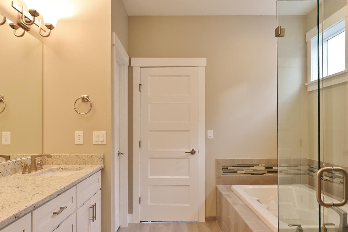 Bathroom with double vanity, five-panel door, and glass-enclosed bathtub and shower area with mosaic tile accent.