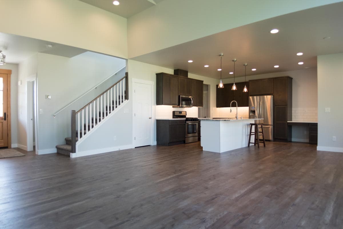 Interior view of an open-concept home with a kitchen island, dark cabinetry, stainless steel appliances, and a staircase.