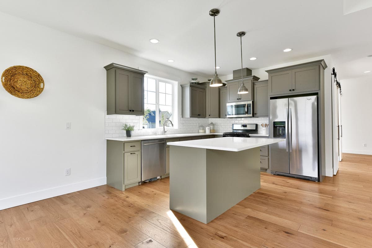 Interior view of a kitchen with gray cabinetry, stainless steel appliances, white subway tile backsplash, and a central island.