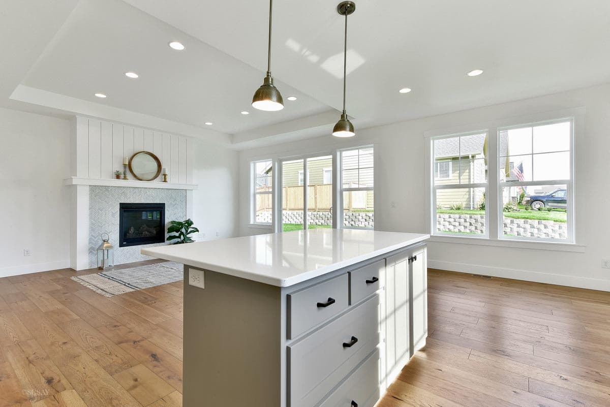Open concept kitchen with island and fireplace, large windows, and tray ceiling.