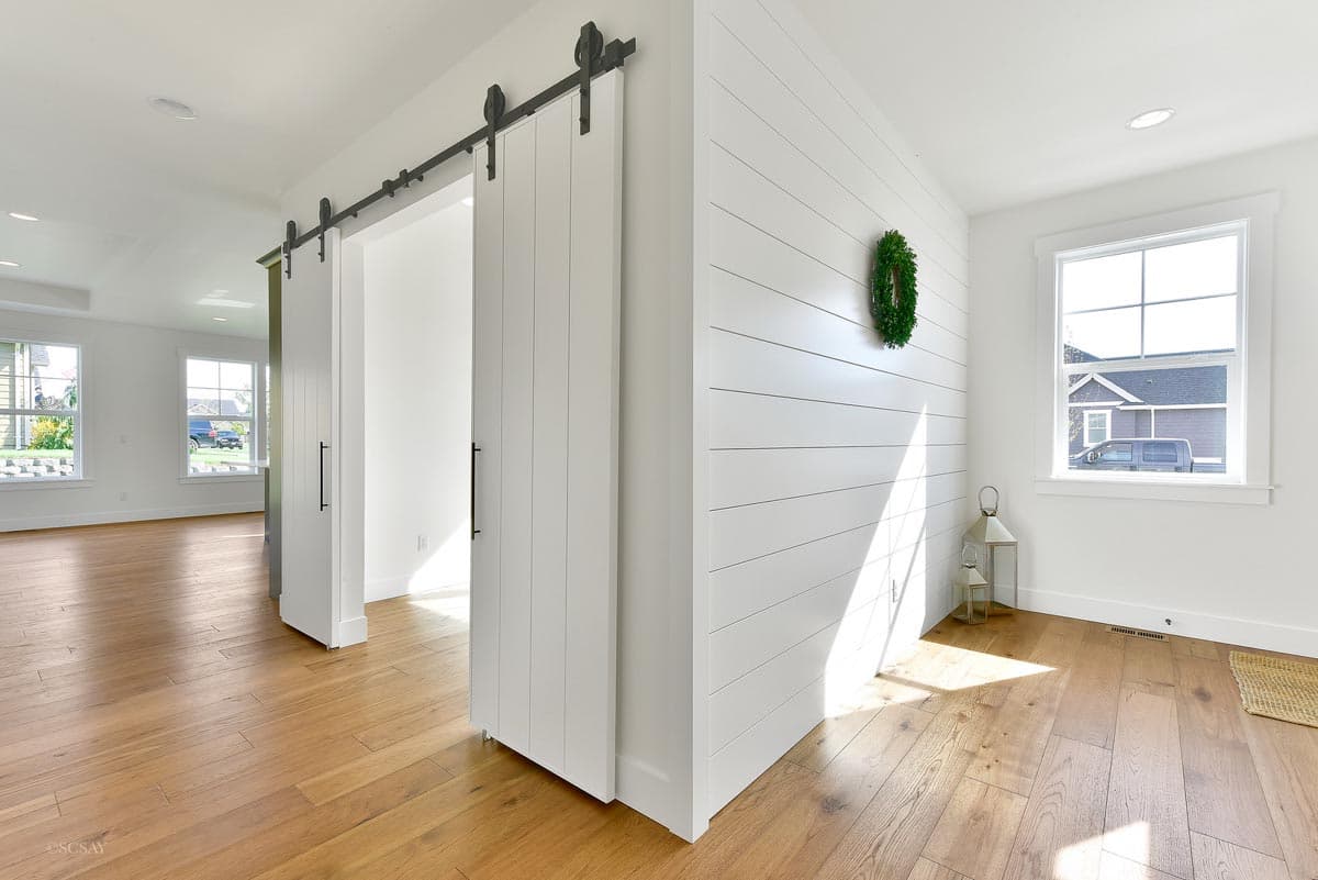 Interior view of a house plan featuring white shiplap walls, barn doors, hardwood floors, and large windows.