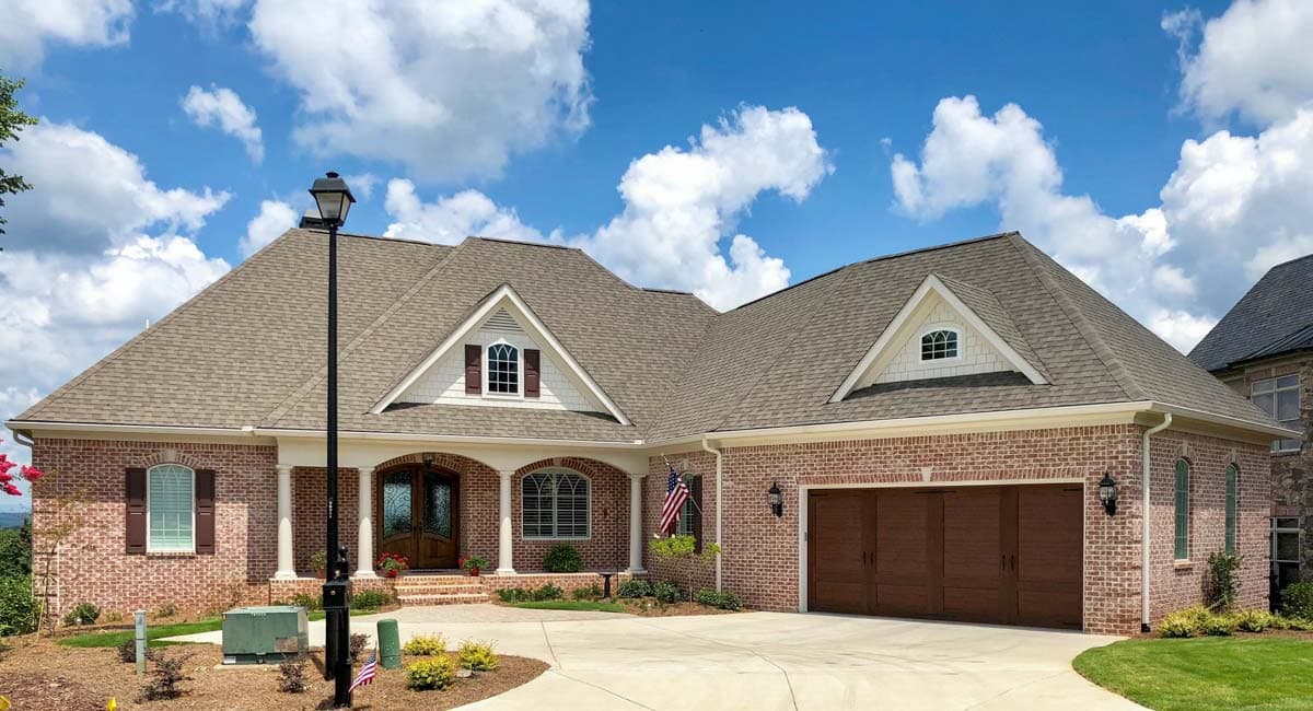 House plan exterior: Brick home with a hip roof, gabled dormers, a covered porch with columns, and a three-car garage.