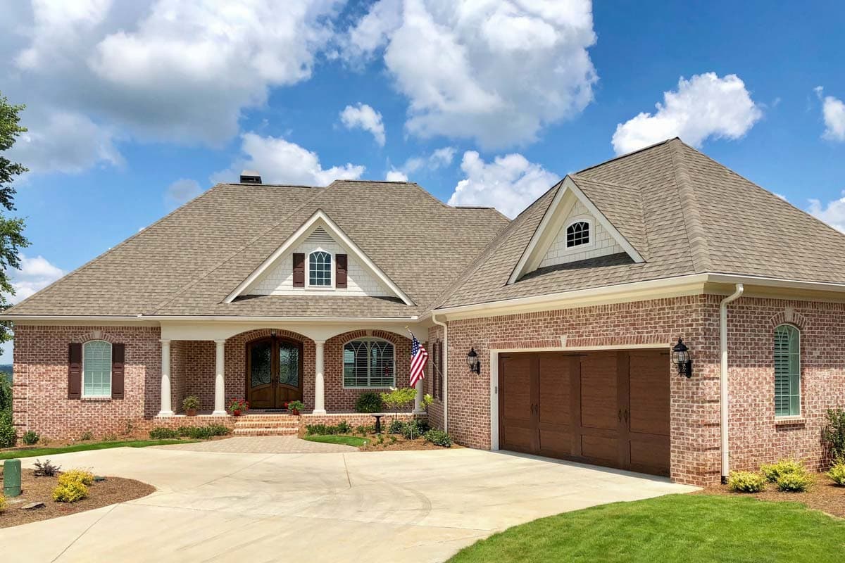House plan exterior. Two-story brick home with gabled roof, arched entry, and attached garage. Includes dormers and a covered porch.