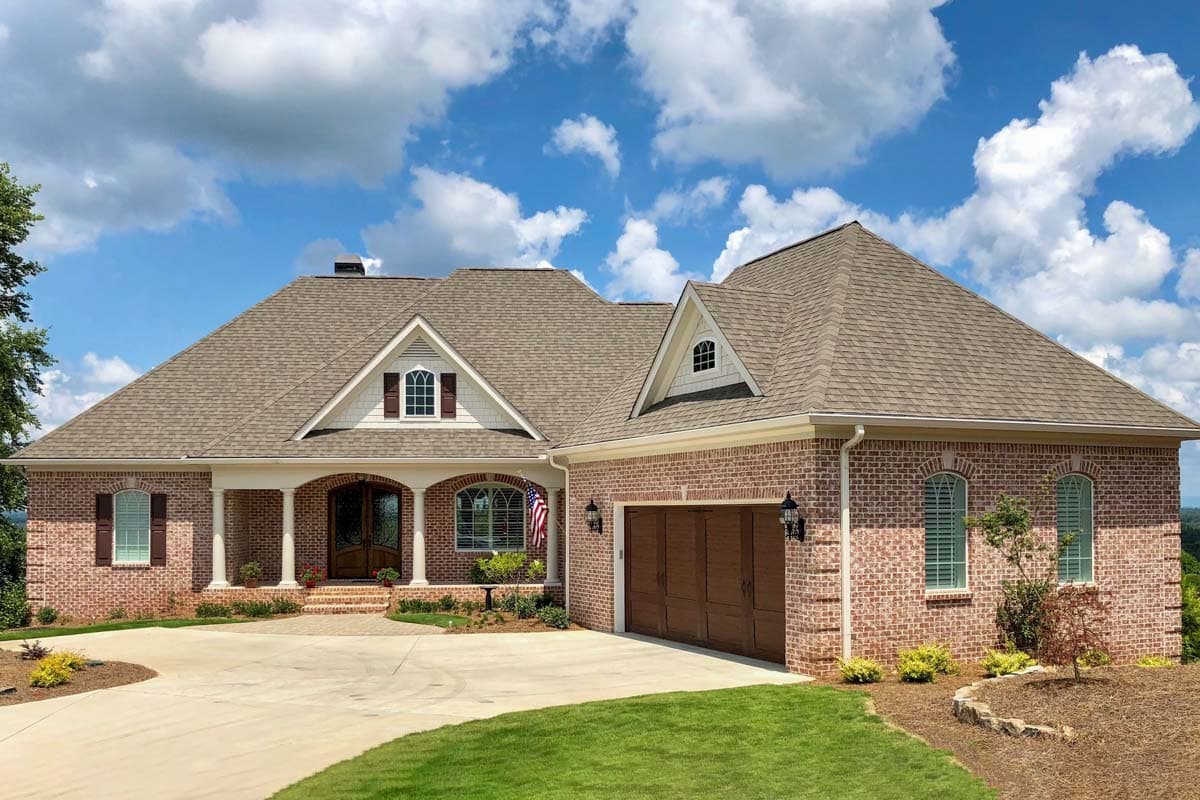 House plan exterior featuring brick facade, arched entryway with columns, dormers, and attached garage.