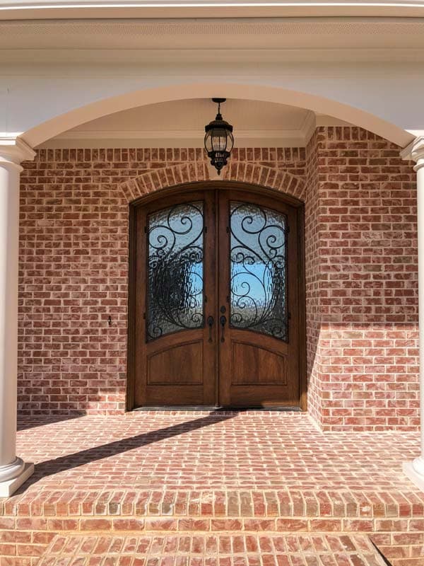 Exterior house plan showing arched double wood doors with decorative glass, brick exterior, and covered porch with columns.