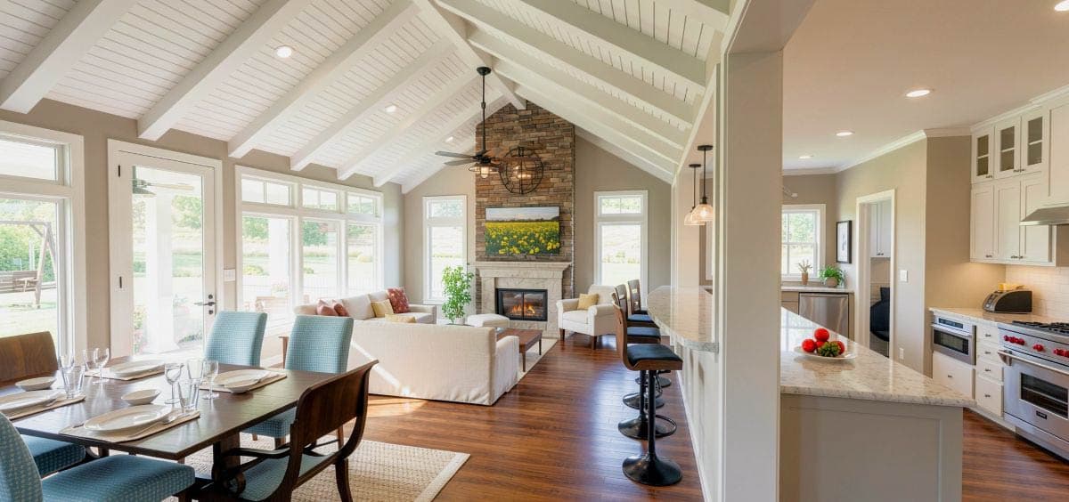 Interior view of a living area with vaulted beamed ceiling, open to a kitchen with island seating and bar stools.