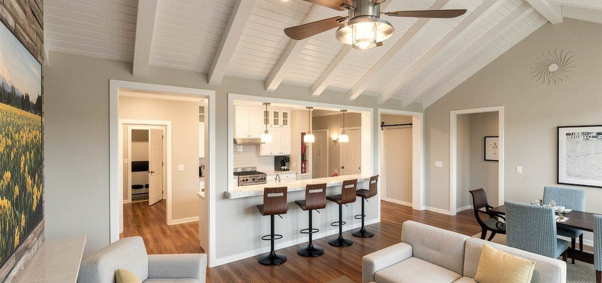 Open concept living area with vaulted beamed ceiling, stone fireplace, dining area, and kitchen with island and bar stools.