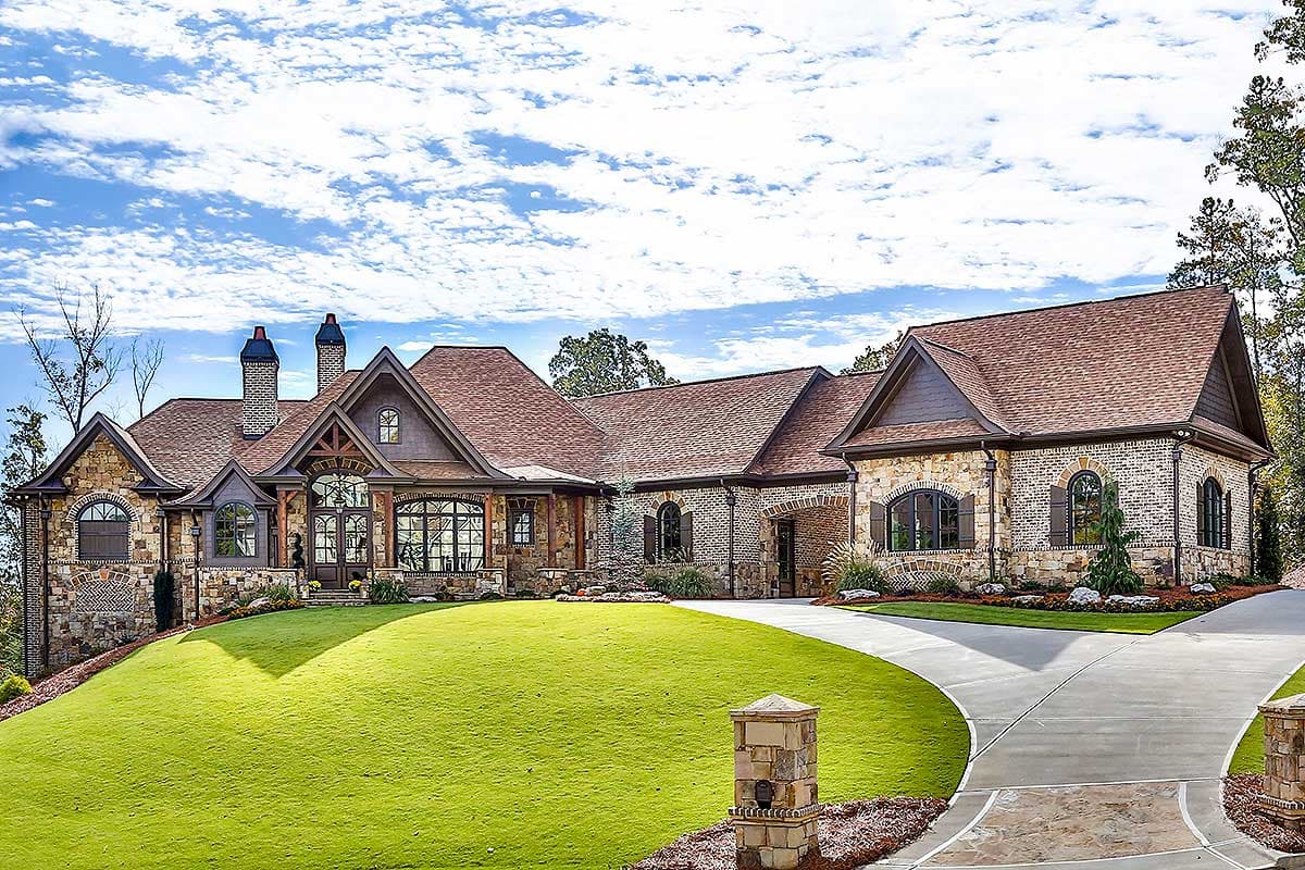 House plan exterior with stone and brick facade, multiple gables, arched windows, and a driveway with a curved entrance.