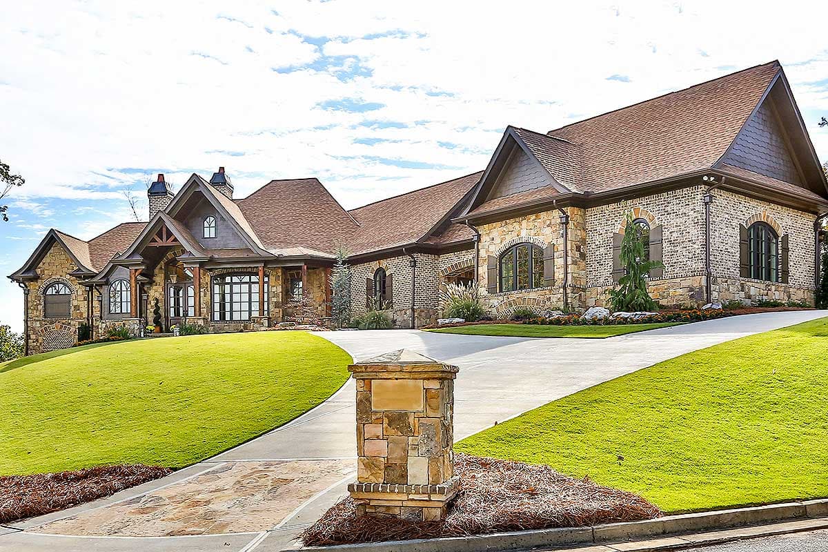 House plan exterior: Stone and brick two-story home with multiple gables, arched windows, and a covered entrance.